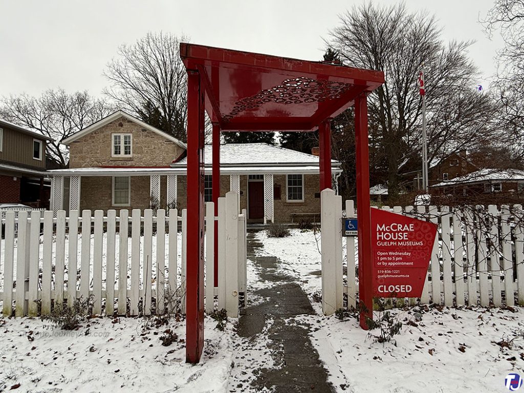 December 23, 2024 – The McCrae House Museum is located at 108 Water St in Guelph, Ontario. This limestone cottage was built in 1858 and served as the home of the McCrae family from 1870 to 1873. It is also the birthplace of Lieutenant-Colonel John McCrae, a doctor, soldier, and poet known for writing "In Flanders Fields." Notice the poppies on the roof of the red metal arbour at the entrance gate